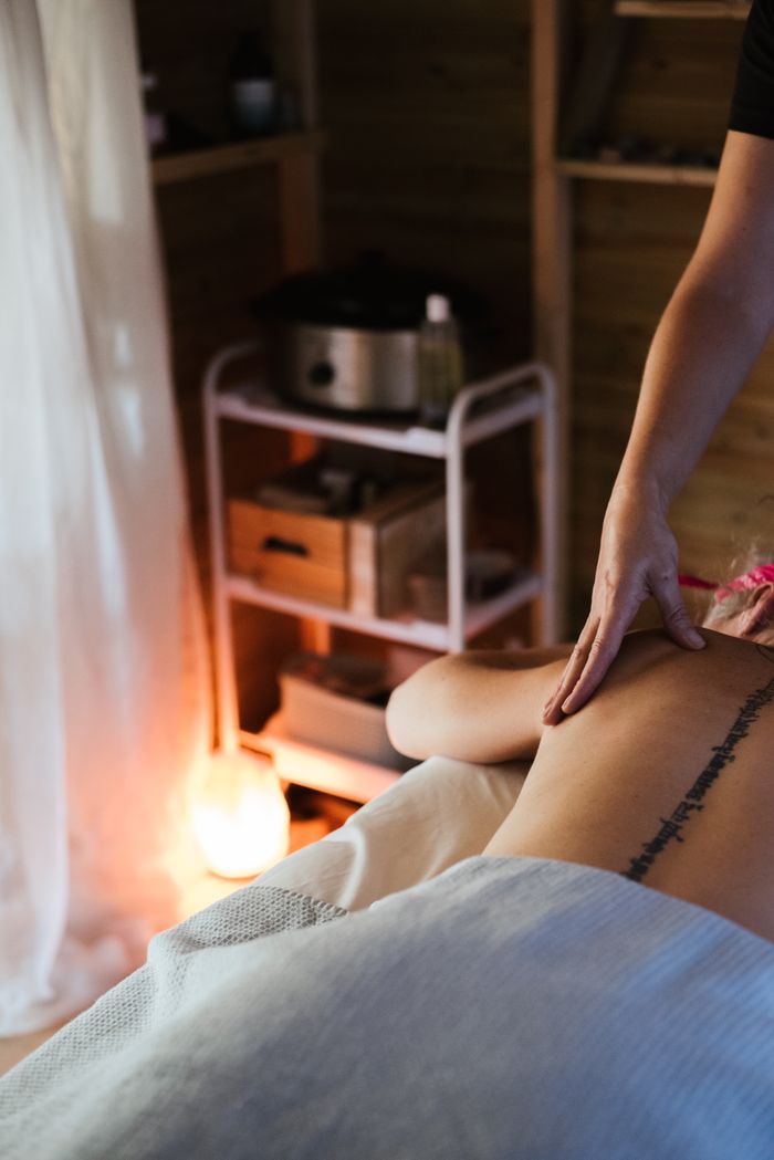 Services Unrecognizable female patient with tattoo on back lying on stomach under blanket while getting massage procedure in cozy spa salon